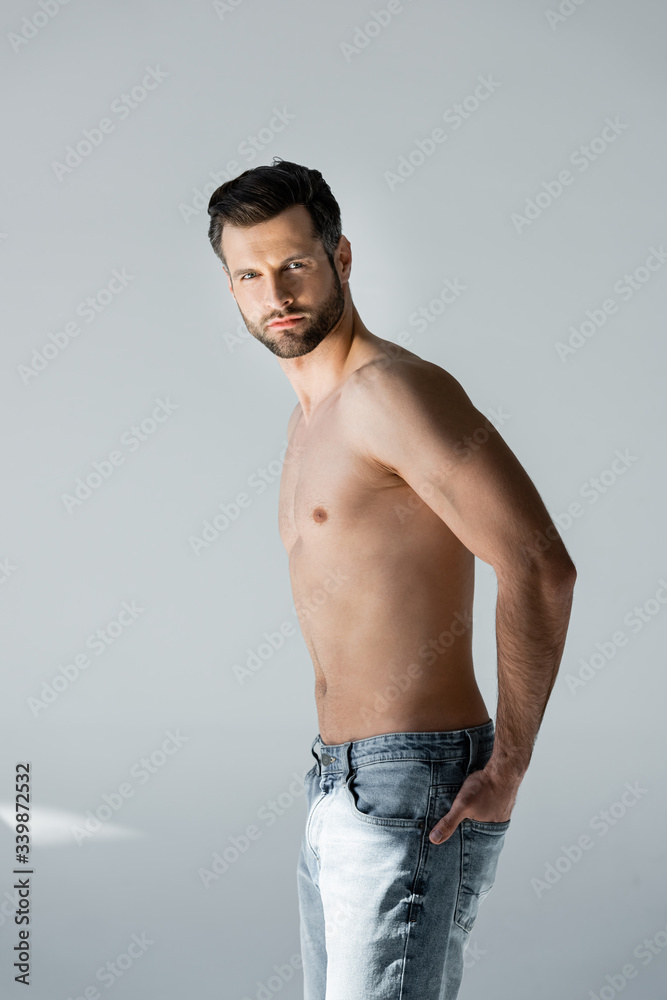 muscular and shirtless man standing with hand in pocket on grey