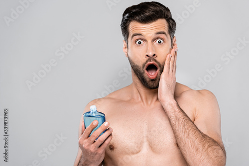 Foto Shocked man holding bottle with after shave lotion and touching face isolated on