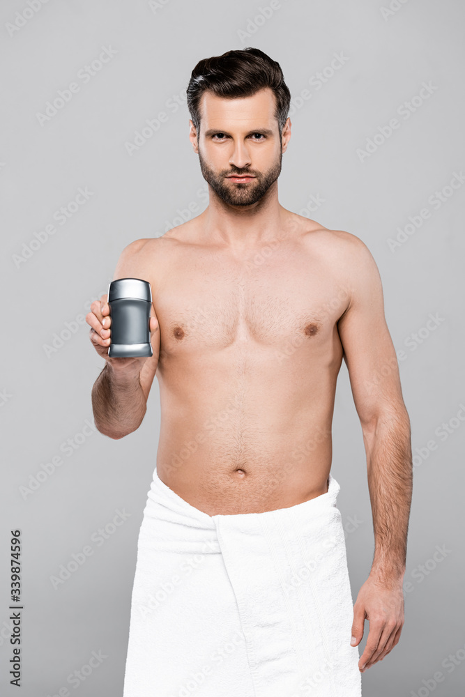 bearded and muscular man in towel holding deodorant isolated on grey bearded and muscular man in towel holding deodorant isolated on grey