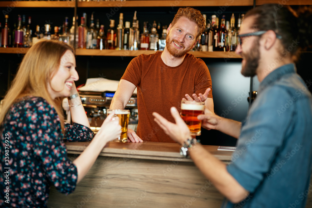 Handsome Caucasian bearded ginger standing in bar with his female friend, drinking beer, chatting and having fun. Pub interior. Nightlife.