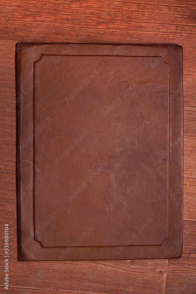 Fototapeta premium Antique brown aged leather cover with different spots on a wooden brown background