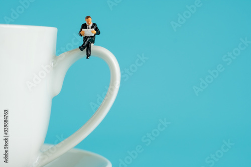 business miniature figures sitting and read a book, read newspaper, waiting, talking and relax on white cup of hot coffee..