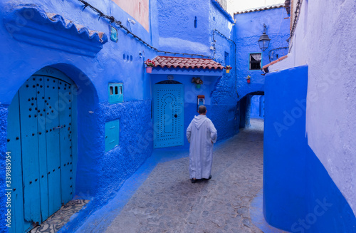 Muslim man with white djellaba walks along the tourist blue street of Chefchaouen. Urban concept. © marcos