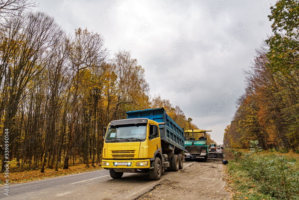 Fototapeta premium Road repair. Laying new asphalt. Heavy special machines. Truck in operation. Side view. Closeup.