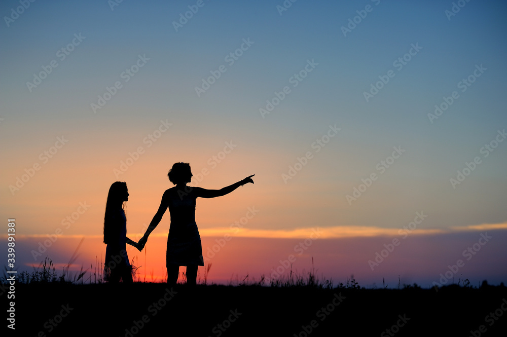 Silhouettes of mother and daughter against the sunset sky.