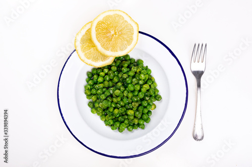 plate of green peas with two slices of lemon and a fork