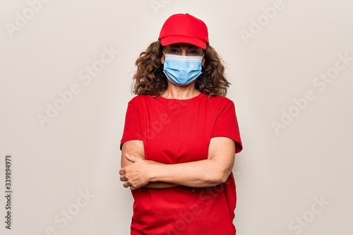 Middle age delivery woman wearing red cap and coronavirus protection mask happy face smiling with crossed arms looking at the camera. Positive person.