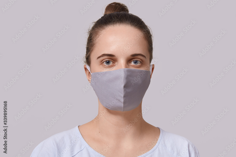 Closeup portrait of serious woman wearing gray protective mask, lady dresses white casual t shirt looking directly at camera, posing isolated over white background. Corona virus protection concept. Closeup portrait of serious woman wearing gray protective mask, lady dresses white casual t shirt looking directly at camera, posing isolated over white background. Corona virus protection concept.