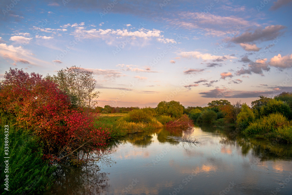 Sunset over the river.  Clouds are reflected in the river at sunset, along the banks of which trees with reddening foliage