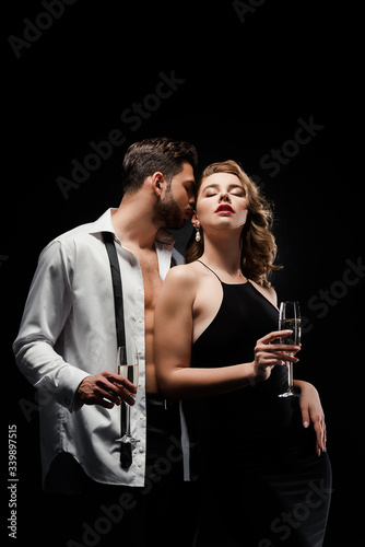 sexy, elegant couple holding champagne glasses while standing isolated on black