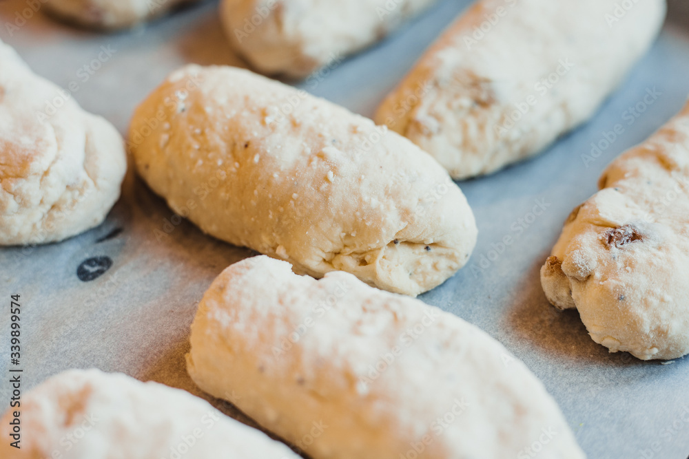 A lots raw curd buns with raisins lie on a baking sheet. Raw dough. Unbaked buns. Selective focus