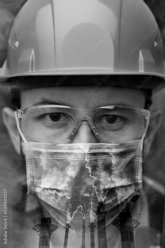 Fototapeta premium Close-up portrait of a worker in a helmet, mask and goggles among smoke and exhaust pipes. Vertical orientation, double exposure.