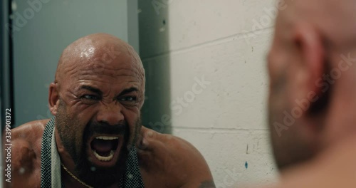 Bald, tan, muscular, bearded man screaming into dirty bathroom mirror.