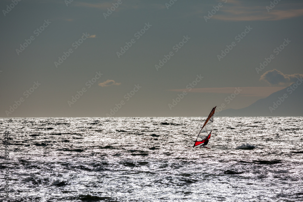 Windy afternoon winter windsurfer silhouette in Thracian sea, seascape landscape, water sports fun, sport, activities, vacation and travel concept. Northern Greece near Porto Lagos village