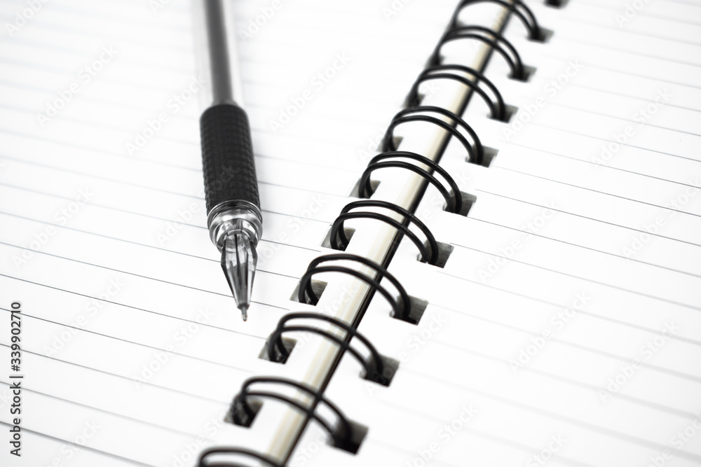 Dark black colored pen placed on top of a simple open white paper diary Dark black colored pen placed on top of a simple open white paper diary