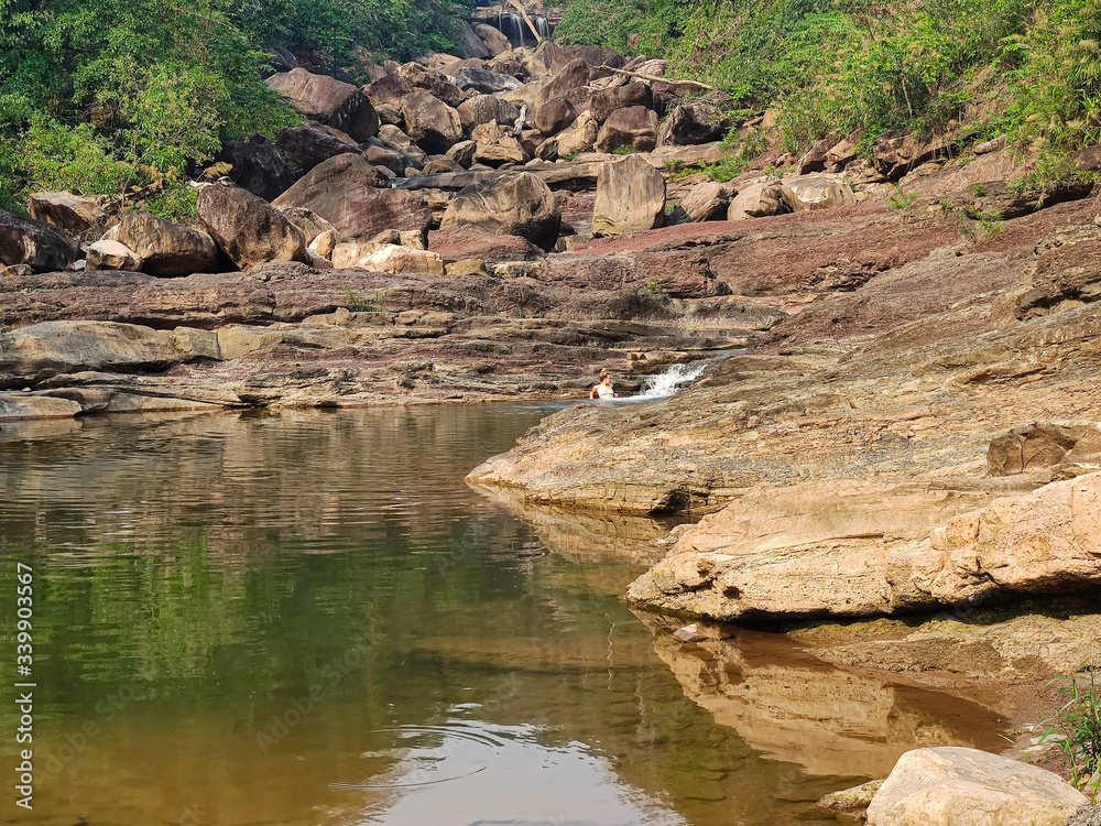 Young female traveler swimming in the dry waterfall. Big rocks with green forest in the jungles.