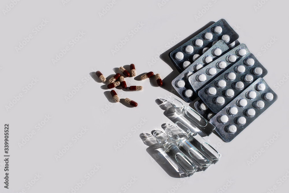 Medicines: white plain breakable tablets in transparent sticks, in metal non-trasparent sticks, overencapsulated tablets, ampuls with anti-virus vaccine on white background. Copy space.