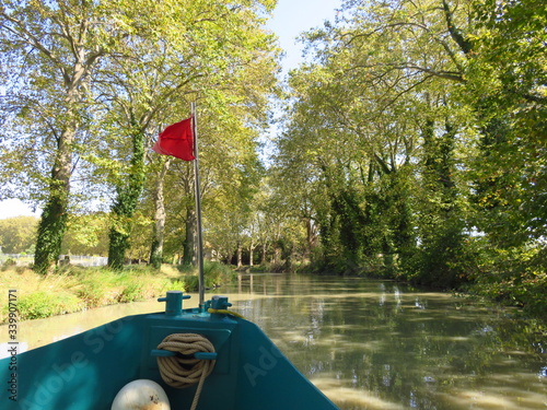 Tourisme fluvial sur le canal du Midi, au milieu des arbres, avec la proue d'un bateau naviguant sur l'eau (France) photo