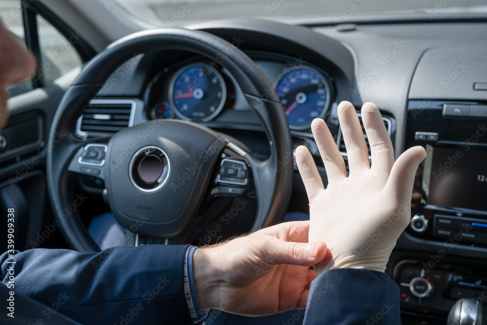 Middle age businessman in blue suit puts on rubber gloves for protect himself from bacteria and virus while driving a car. Coronavirus. Pandemic