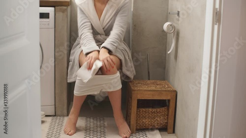 Young caucasian woman in bathrobe sitting on toilet bowl in the morning.