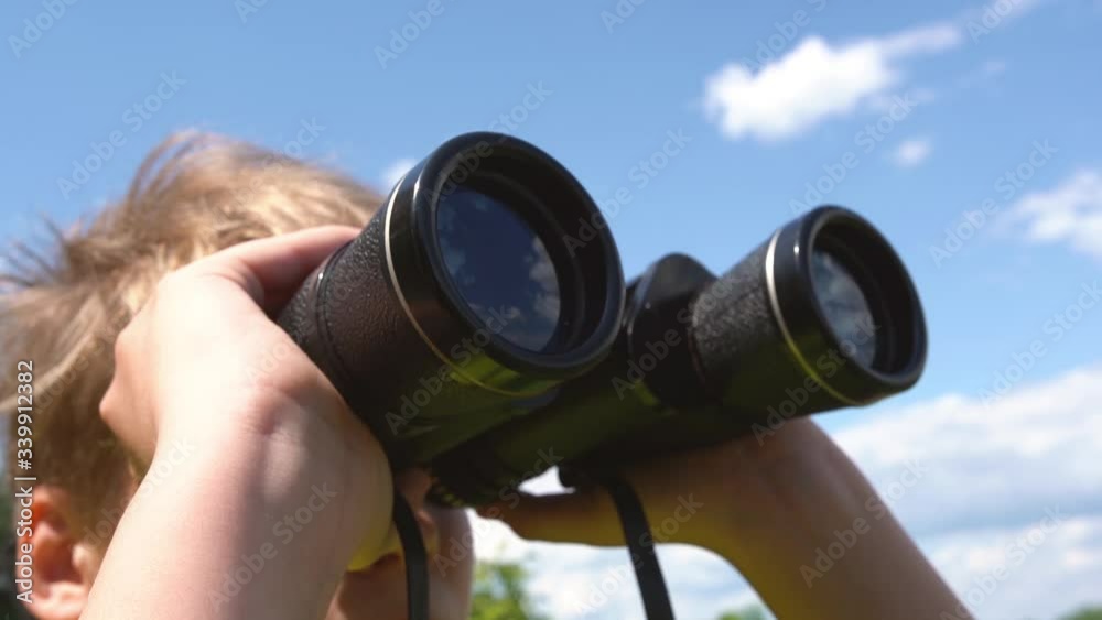 Closeup view video of cute white young kid looking through old black binoculars standing in sunny summer countryside landscape. Closeup view video of cute white young kid looking through old black binoculars standing in sunny summer countryside landscape.