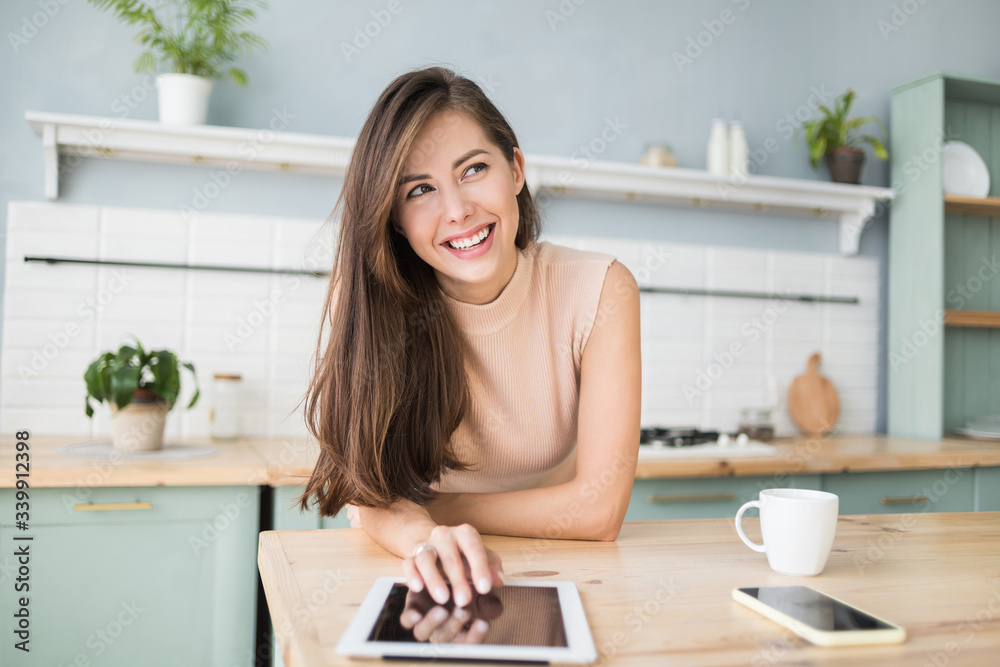Beautiful young woman with digital tablet relaxing at home, Happy student girl using tablet pc in kitchen, Resting, relaxation, technology, online shopping, studying at home, learning online concept Beautiful young woman with digital tablet relaxing at home, Happy student girl using tablet pc in kitchen, Resting, relaxation, technology, online shopping, studying at home, learning online concept