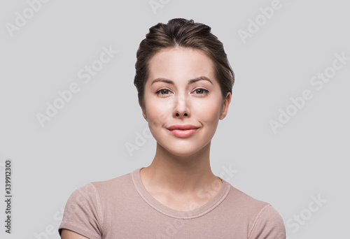 Beautiful young woman studio closeup portrait. Smiling girl looking at camera isolated on gray background. Model with perfect clean skin. Beauty  makeup  healthy lifestyle and skin care concept