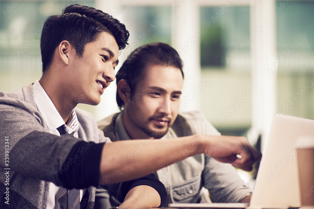 two young asian business men working together in office using laptop computer two young asian business men working together in office using laptop computer