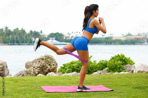 Fitness woman doing kickback exercise for glute with resistance band, outdoors. Athletic girl workout photo