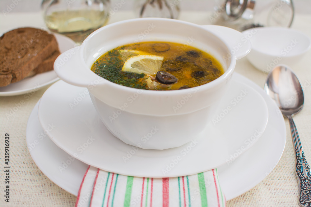 Traditional Russian meat soup solyanka with sausages, lemon and olives in a white ceramic bowl. Traditional Russian meat soup solyanka with sausages, lemon and olives in a white ceramic bowl.