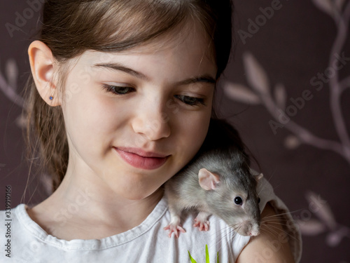 Cute little  girl holding a decorative rat. Animal, pets and children concept. Friendship of children and animals.
Rat on the shoulder.
