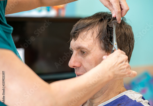 Self hair care at home during quarantine. A woman cutting hair of mid adult man's hair at home in room. Selective focus.