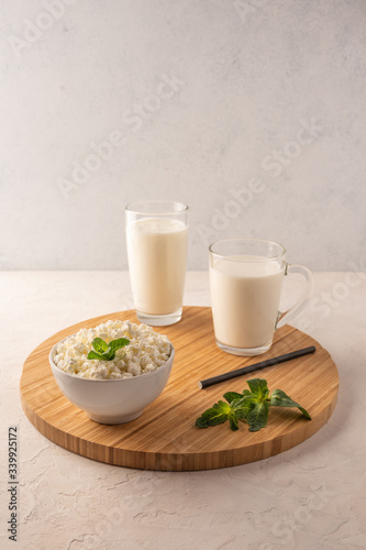 Milk in a cup, kefir in a glass and cottage cheese with herbs in a bowl on a wooden tray on a light background. Copy space