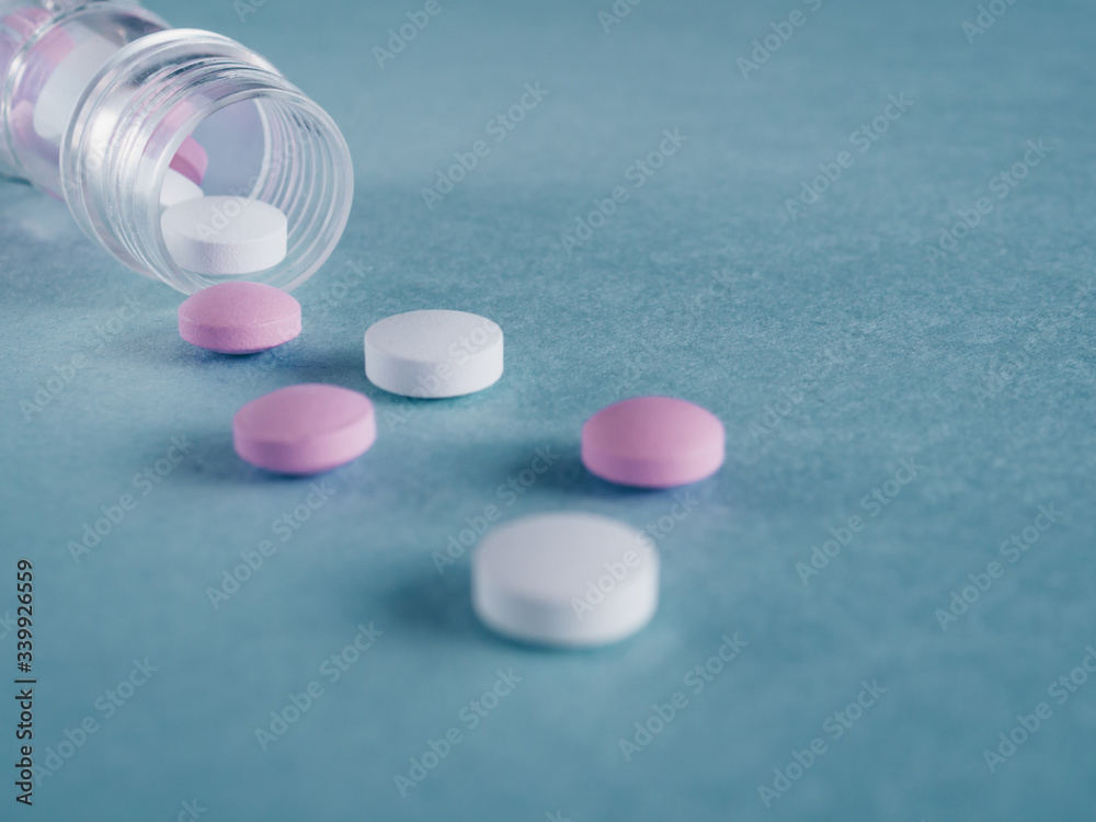 Group of pink and white round medicine pills and bottle on a blue background. Selective focus. Shallow depth of field. Theme of health care, medical treatment and disease prevention. Group of pink and white round medicine pills and bottle on a blue background. Selective focus. Shallow depth of field. Theme of health care, medical treatment and disease prevention.