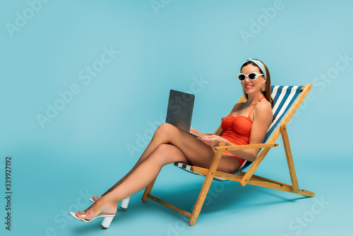 Foto Freelancer with crossed legs and laptop smiling on deckchair on blue