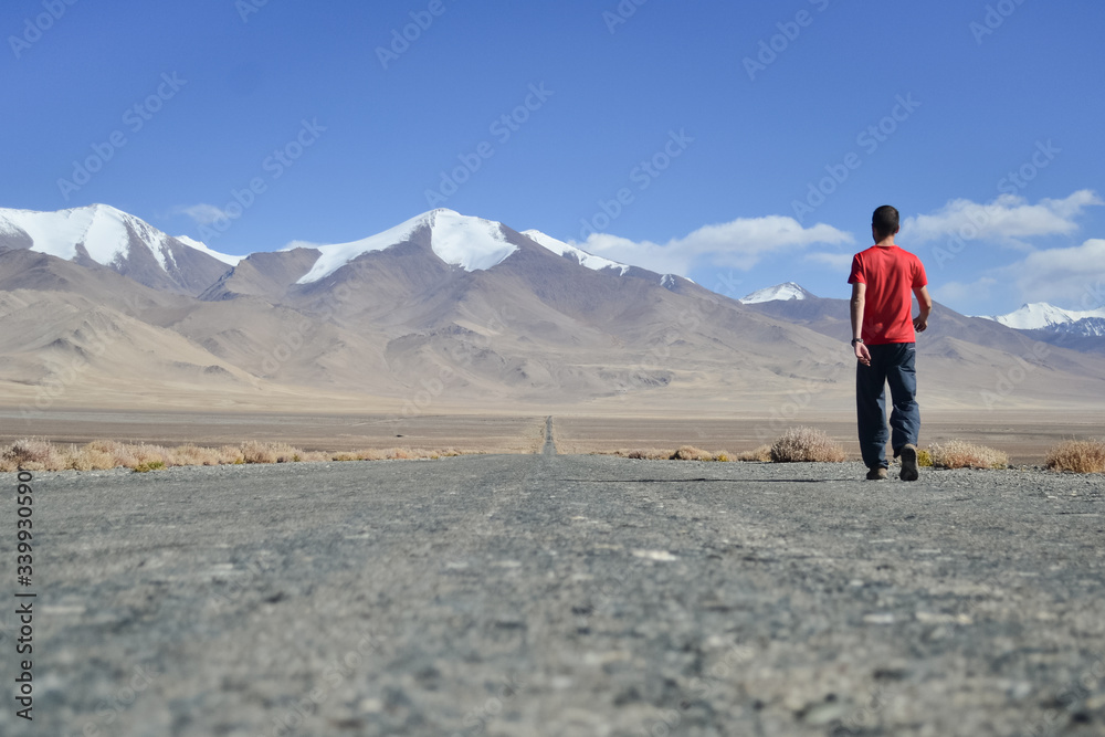 Scenery gravel road with snow peaks mountains in the background and a man walking away