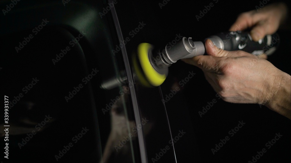 Car detailing - Hands with orbital polisher in auto repair shop. Selective focus. Car polishing and LCP correction