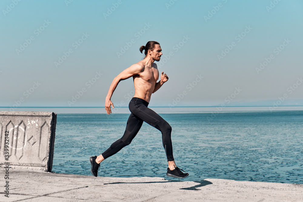Side view of Topless Healthy Handsome Active Man running on sidewalk in morning At Sea. Health conscious concept with copy space. Side view of Topless Healthy Handsome Active Man running on sidewalk in morning At Sea. Health conscious concept with copy space.