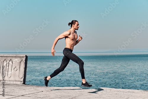 Side view of Topless Healthy Handsome Active Man running on sidewalk in morning At Sea. Health conscious concept with copy space.