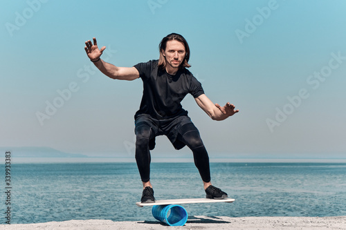 Closeup Of Healthy Handsome Active Man With Fit Muscular Body keeping balance on the wooden board against the background of sea on summer day