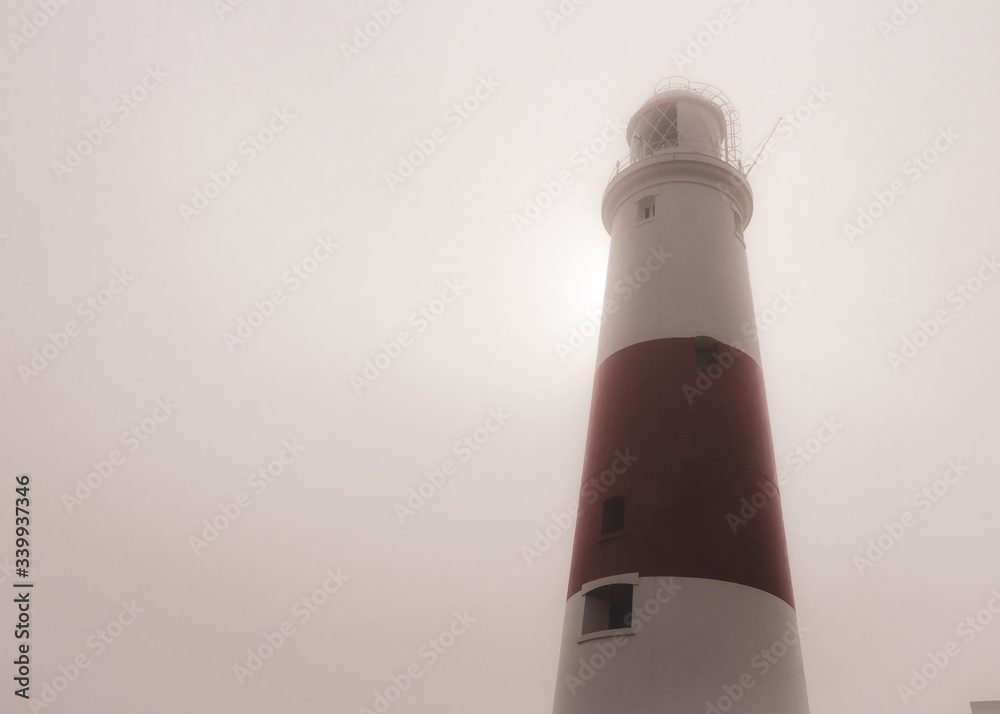 Portland Bill lighthouse on a foggy summer morning as the sun tries to break through behind, Portland, Dorset, UK