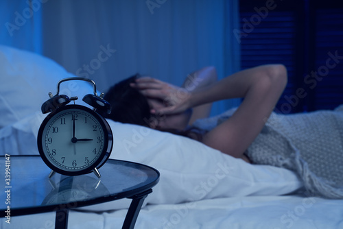 Unhappy woman with insomnia lying on bed next to alarm clock at night photo