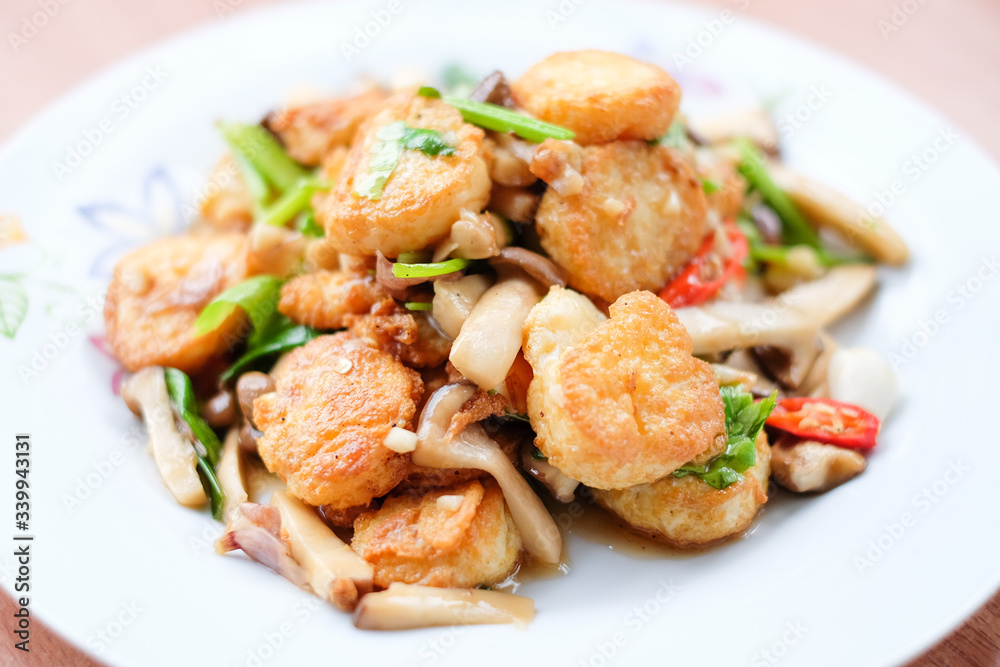 The hot stir fried tofu and pork and mushroom with black bean sauce serve on white dish set on brown table - homemade food concept. The hot stir fried tofu and pork and mushroom with black bean sauce serve on white dish set on brown table - homemade food concept.