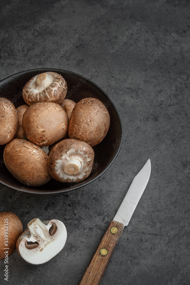 Braune Champignons in einer Schüssel zusammen mit einem Messer auf einem dunklen Hintergrund