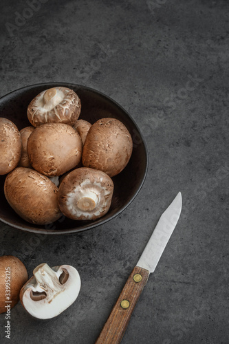 Obraz na płótnie Braune Champignons in einer Schüssel zusammen mit einem Messer auf einem dunklen Hintergrund w salonie