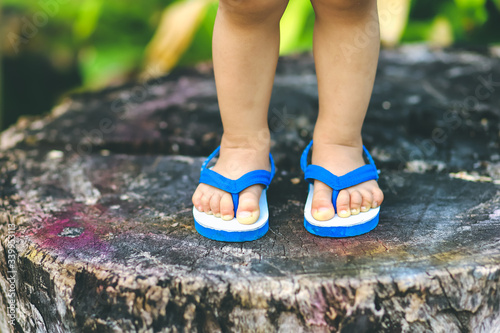 Close up kid feet with casual white and blue sandals standing on wood log