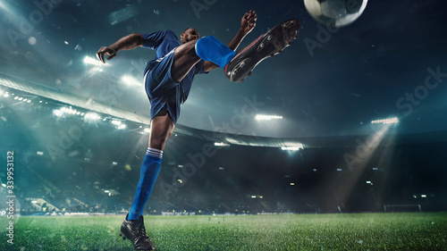 Professional football or soccer player in action on stadium with flashlights, kicking ball for winning goal, wide angle. Concept of sport, competition, motion, overcoming. Field presence effect.