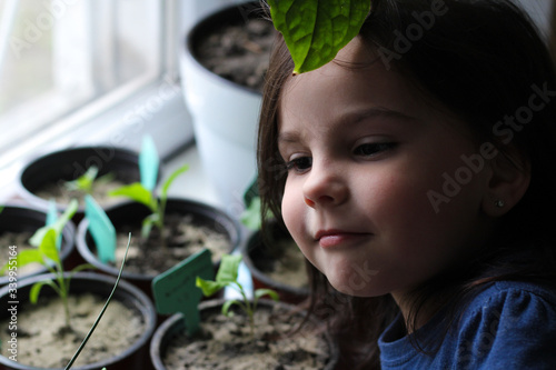 Portrait of a little white girl near potted seedlings growing on a windowsill