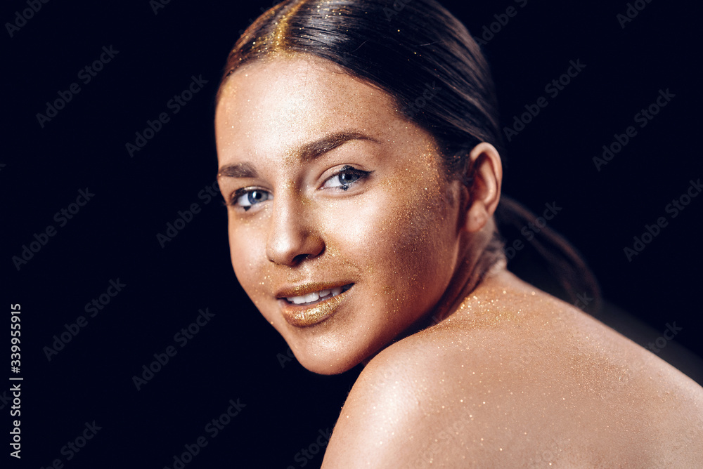 Fototapeta premium Beauty fashion art model girl with Golden skin. Close up portrait of girl with blue eyes on black background