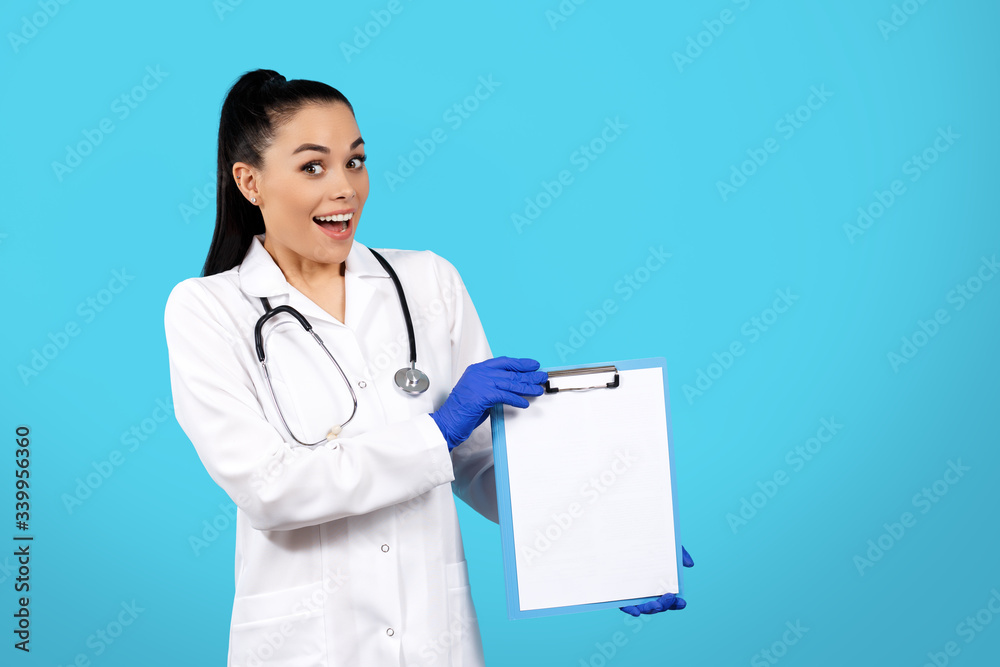 Portrait of excited pretty young woman doctor with stethoscope holding clipboard over blue background. Portrait of excited pretty young woman doctor with stethoscope holding clipboard over blue background.